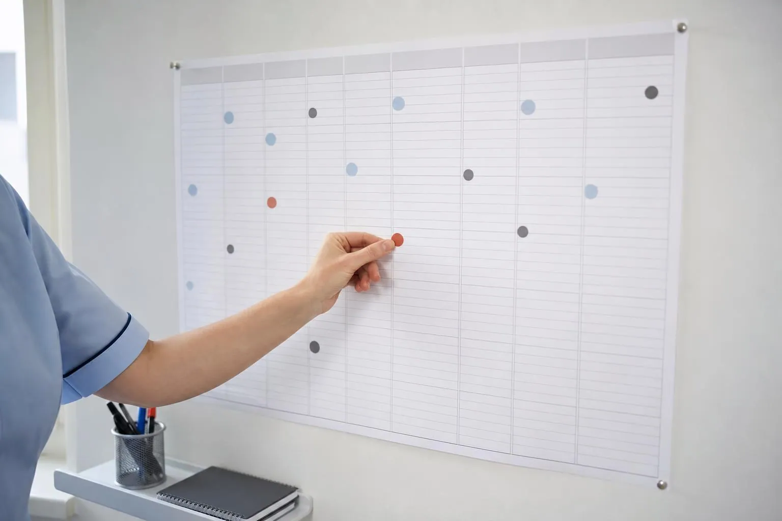 Calendrier mural annuel en papier fixe au mur d'un cabinet, une main y posant une pastille adhesive de couleur