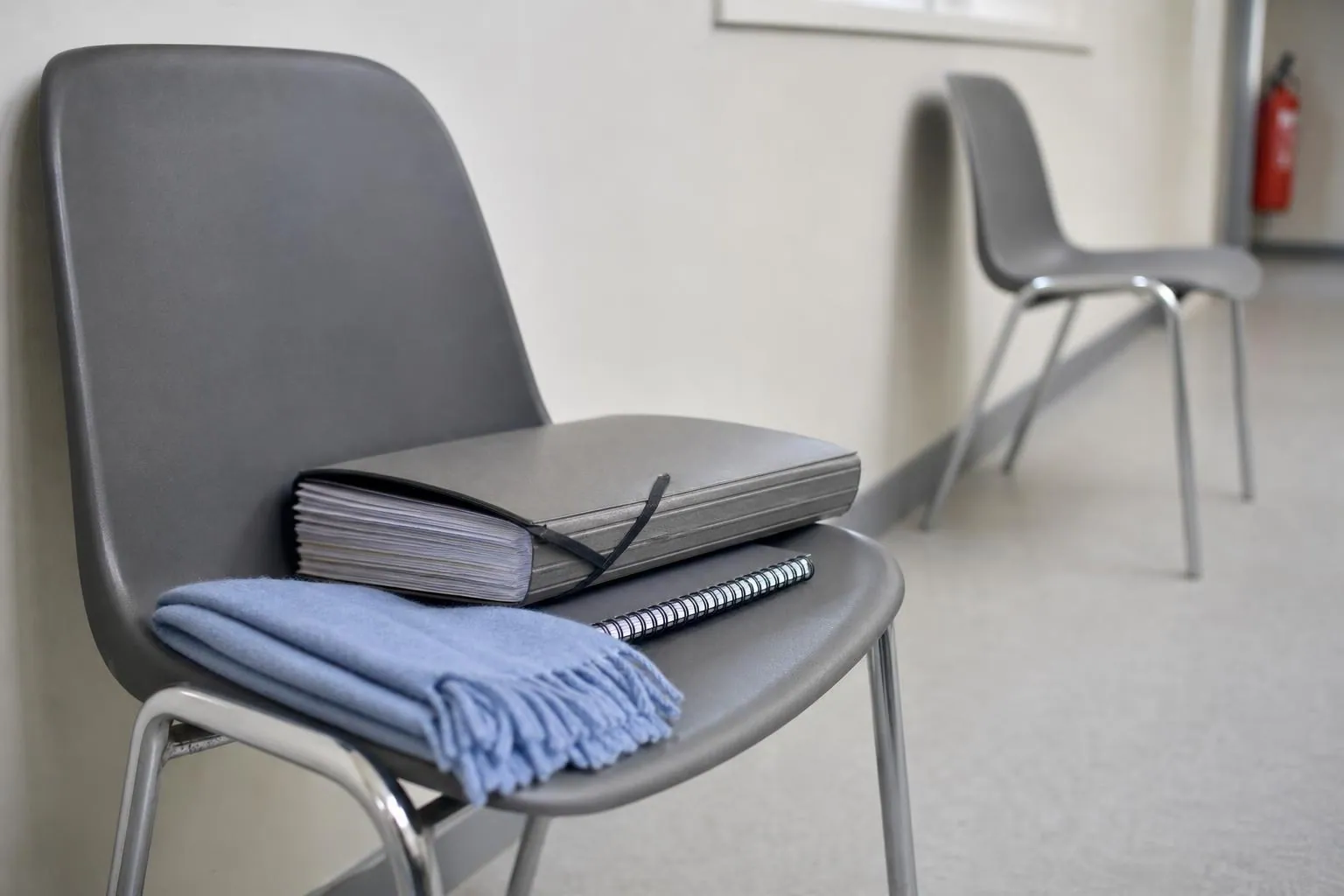 Pochette cartonnee a elastiques remplie de documents, posee sur une chaise dans un couloir d'immeuble administratif clair