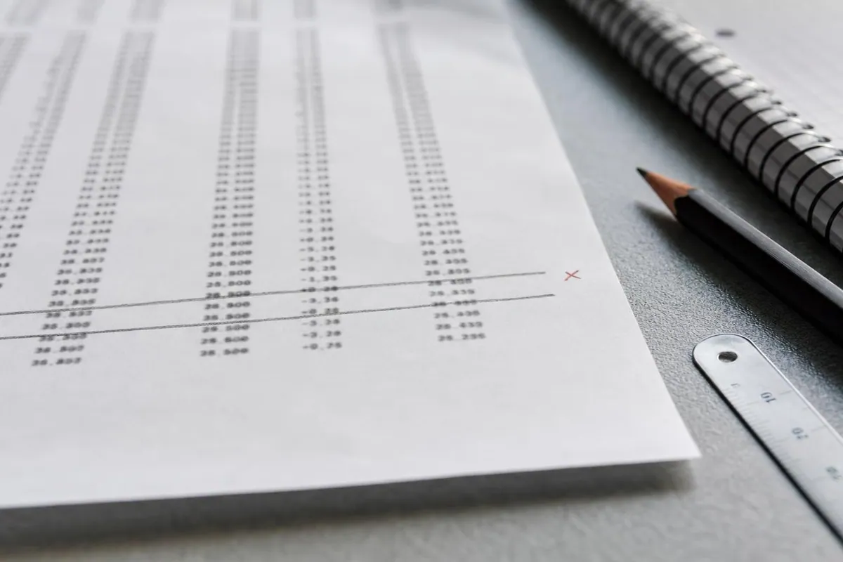 Gros plan d'une feuille de releve d'honoraires imprimee et annotee au crayon, posee sur un plan de travail clair a cote d'un carnet de tournee
